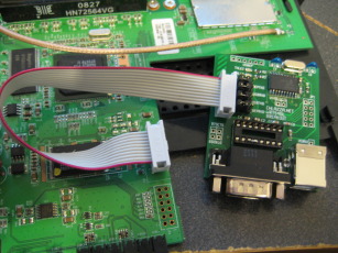 Photo of WRT54GL breakout board plugged into router mainboard via ten pin ribbon cable.
